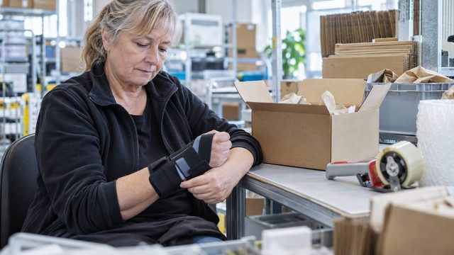 Frau mit Handschiene an einem Packtisch während einer Arbeitserprobung trotz Erwerbsminderungsrente