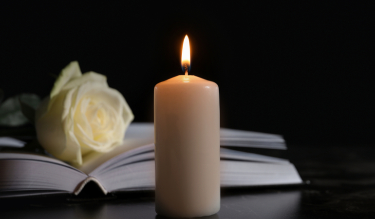 Brennende Kerze vor einem Buch mit einer weißen Blume