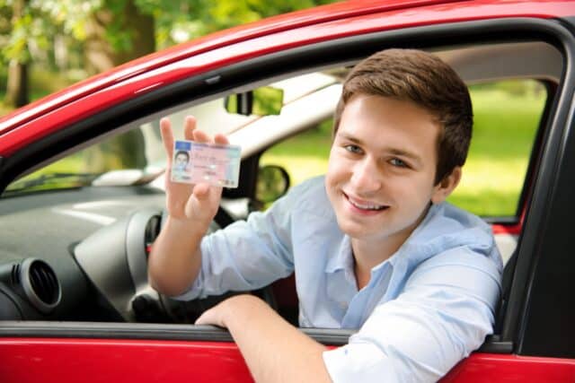 Mann sitzt im Auto und hält Führerschein hoch