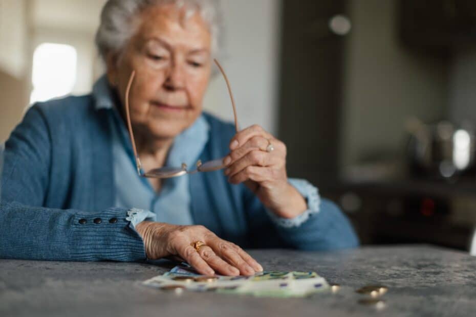 Besorgte ältere Dame am Esstisch, die auf Grundsicherung angewiesen ist und ihr Geld zählt