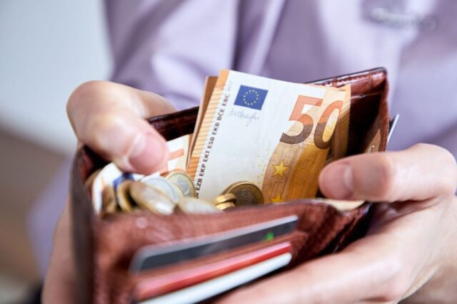 Person hält Portemonnaie mit Bargeld und Euro-Münzen.