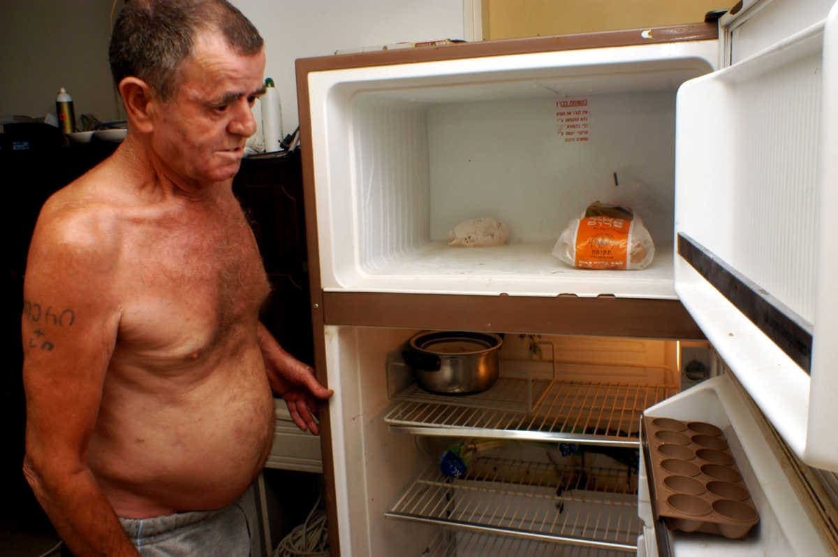 Armer älterer Mann vor einem leeren Kühlschrank