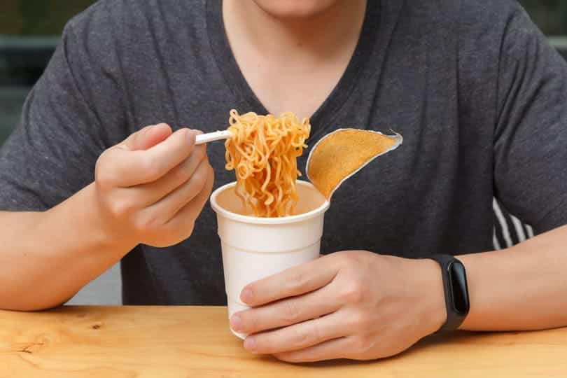 junger Mann isst Tütensuppe aus dem Pappbecher