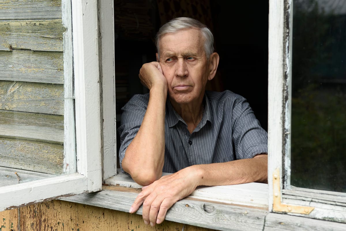 Rentner sitzt frustriert am offenen Fenster