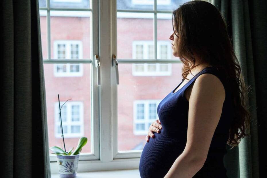 Schwangere Frau schaut traurig aus dem Fenster