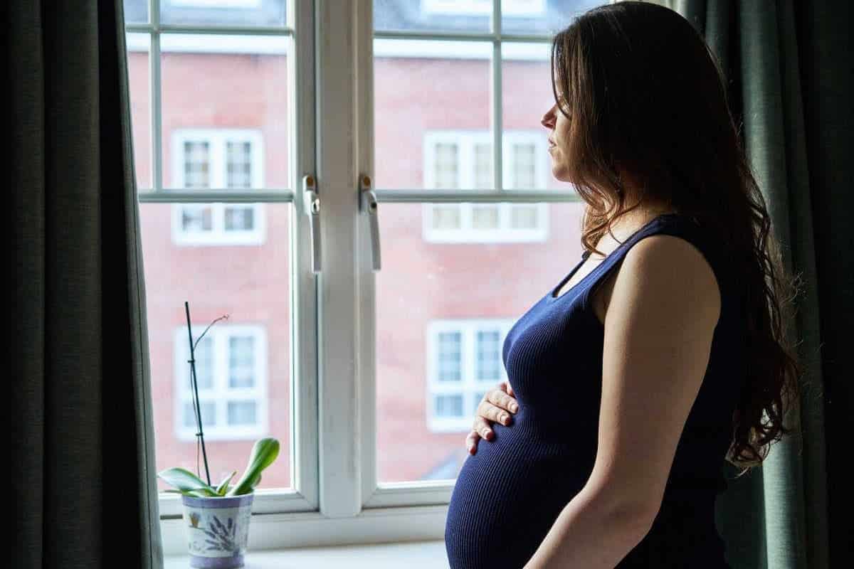 Schwangere Frau schaut traurig aus dem Fenster