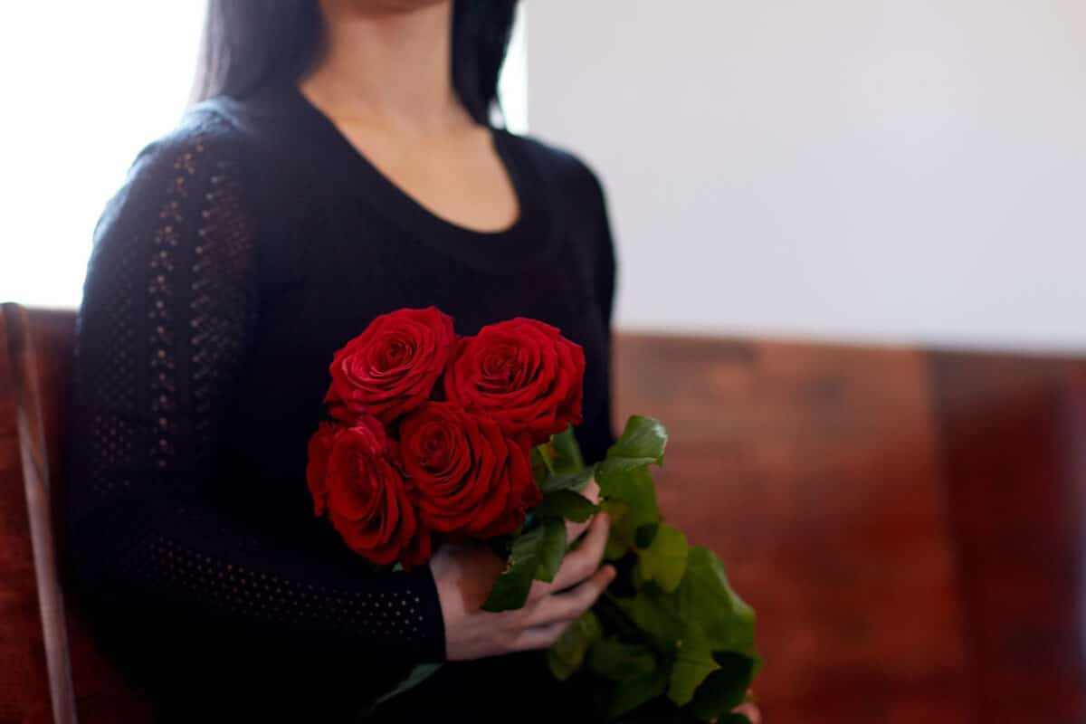 Witwe sitzt auf Kirchenbank und hält einen Strauß Rosen