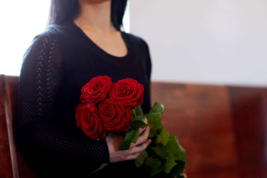 Witwe sitzt auf Kirchenbank und hält einen Strauß Rosen