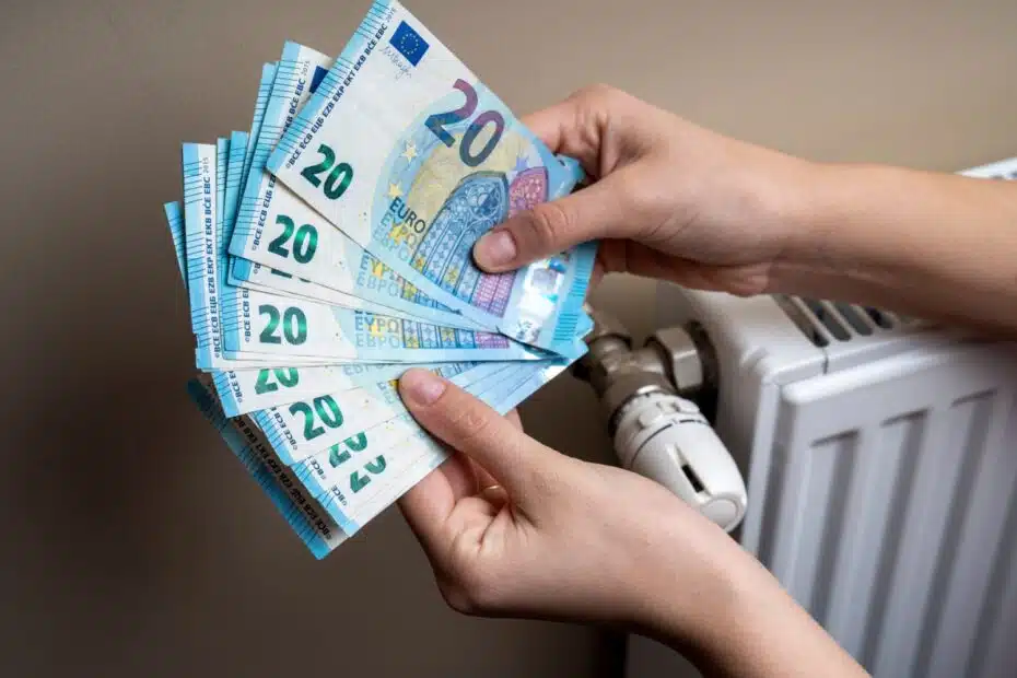 Hände neben einem Heizkörper, halten 20 Euro Geldscheine - symbolisch für Heizkosten