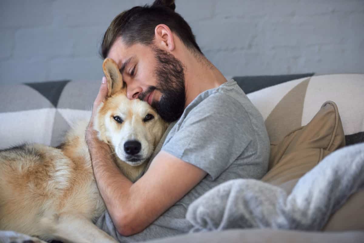 Mann kuschelt mit Hund auf Sofa