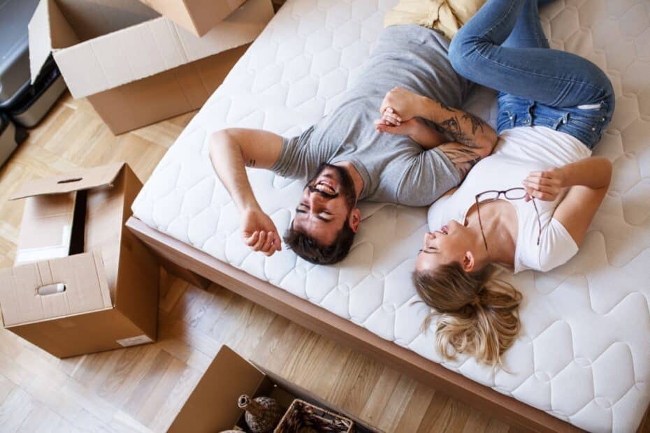 Junges Paar liegt zufrieden auf dem Bett, drumherum stehen Umzugskartons