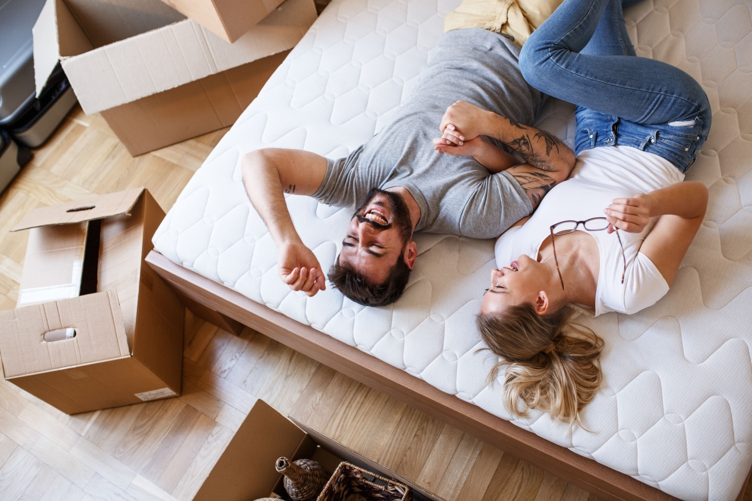 Junges Paar liegt zufrieden auf dem Bett, drumherum stehen Umzugskartons