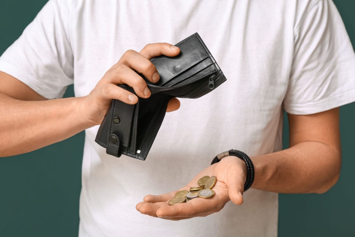 Mann hält leeres Portemonnaie in der Hand und zählt einige Münzen – Symbolbild für finanzielle Not und Bürgergeld-Aufstockung durch das Jobcenter.