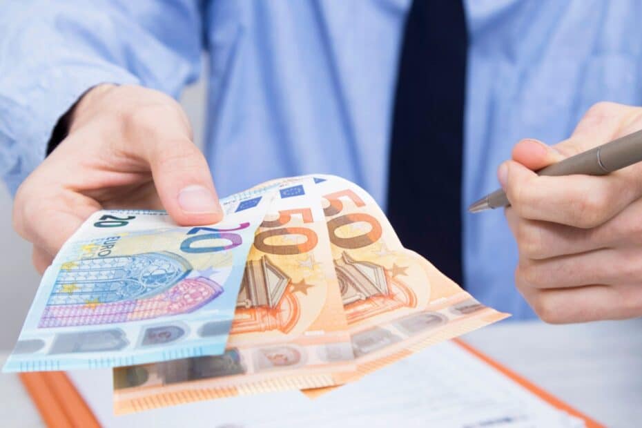 Hand reicht Geldscheine über Formularen und hält in der anderen einen Kugelschreiber, symbolisch für Darlehen beantragen