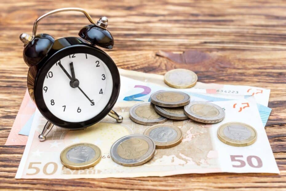 Kleiner Wecker steht auf Geldschreinen und Münzen, symbolisch für Fristablauf für Bürgergeld-Anspruch