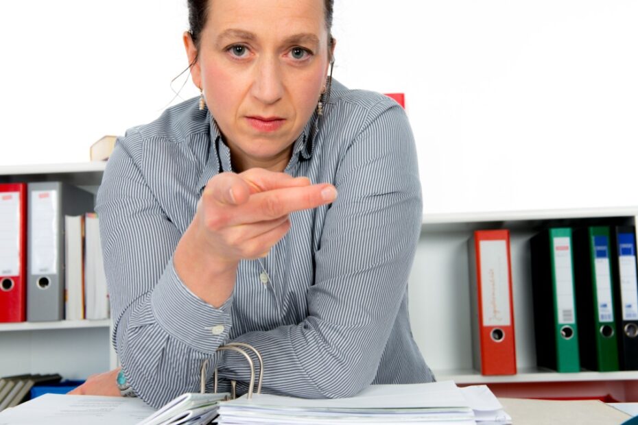 Jobcenter Sachbearbeiterin mit forderndem Blick und zeigendem Finger. Themenschwerpunkt: Bürgergeld Vermittlungsvorschläge.