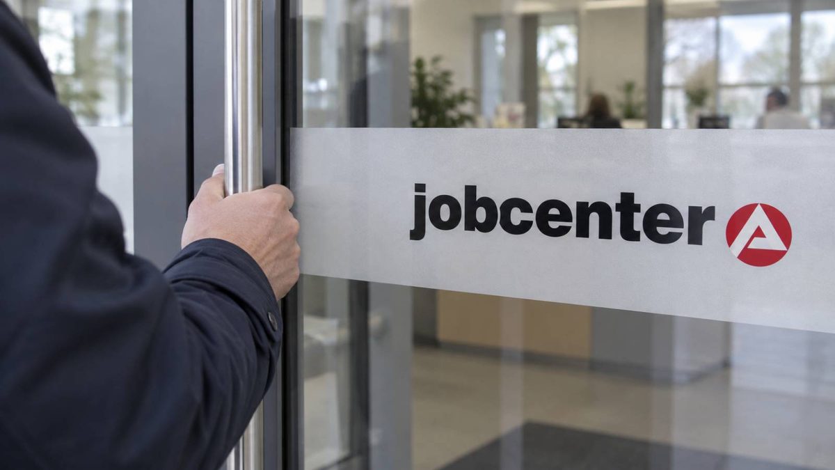 Ein Mann öffnet die Glastür zum Eingang eines Jobcenters.
