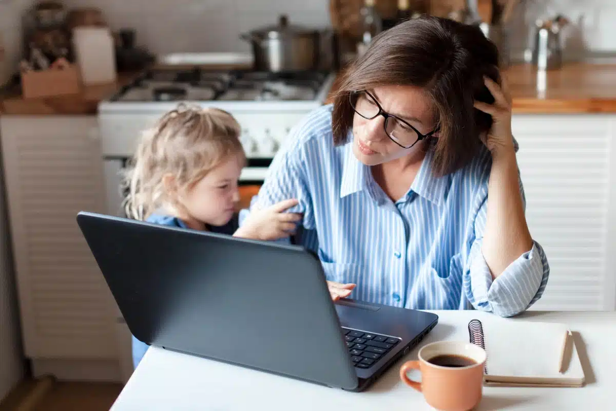 Alleinerziehende Mutter sitzt mit ihrem Kind am Laptop und prüft ihre Bürgergeld-Zahlung vom Jobcenter.
