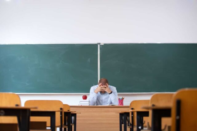 junger Lehrer im leeren Klassenraum vor Tafel