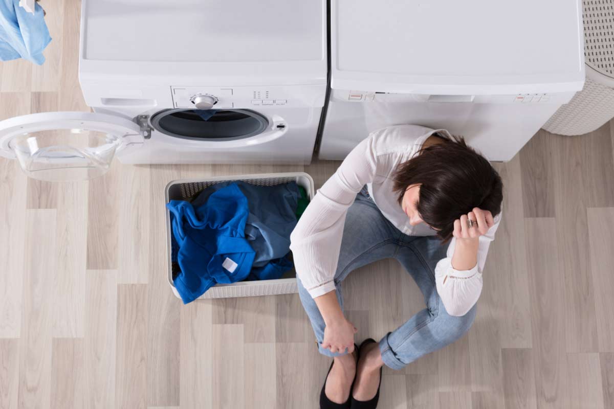 Traurige Frau sitzt vor Waschmaschine