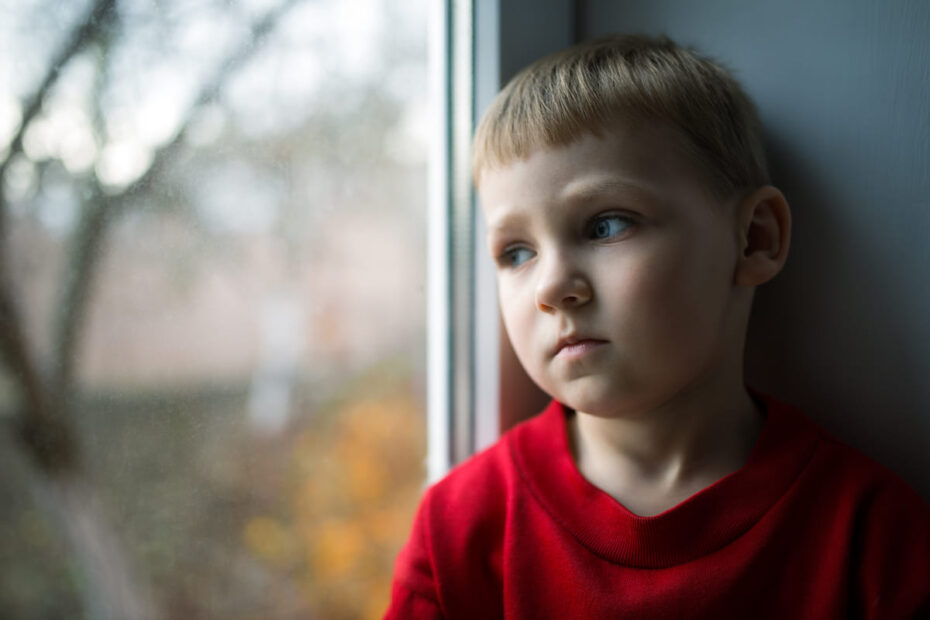 Trauriger Junge in Armut lebend schaut aus Fenster