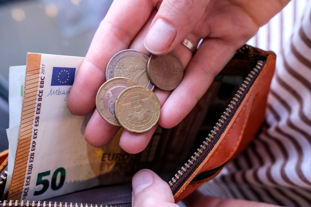 Nahaufnahme einer Person, die in einem braunen Lederportemonnaie nach Euromünzen sucht; im Hintergrund ist ein Geldschein sichtbar. Symbolbild zur Kindergelderhöhung 2026 und finanzieller Knappheit.