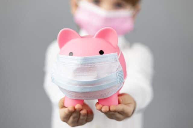 Kind mit Sparschwein und Corona-Maske