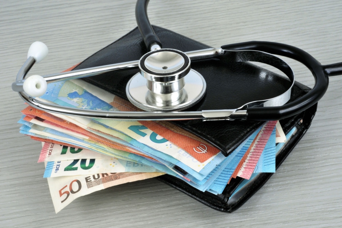 Stethoskop liegt auf einem Stapel Euro-Banknoten und einer schwarzen Geldbörse. Symbolisiert die hohen Gesundheitskosten und Belastung für die Krankenkassen.