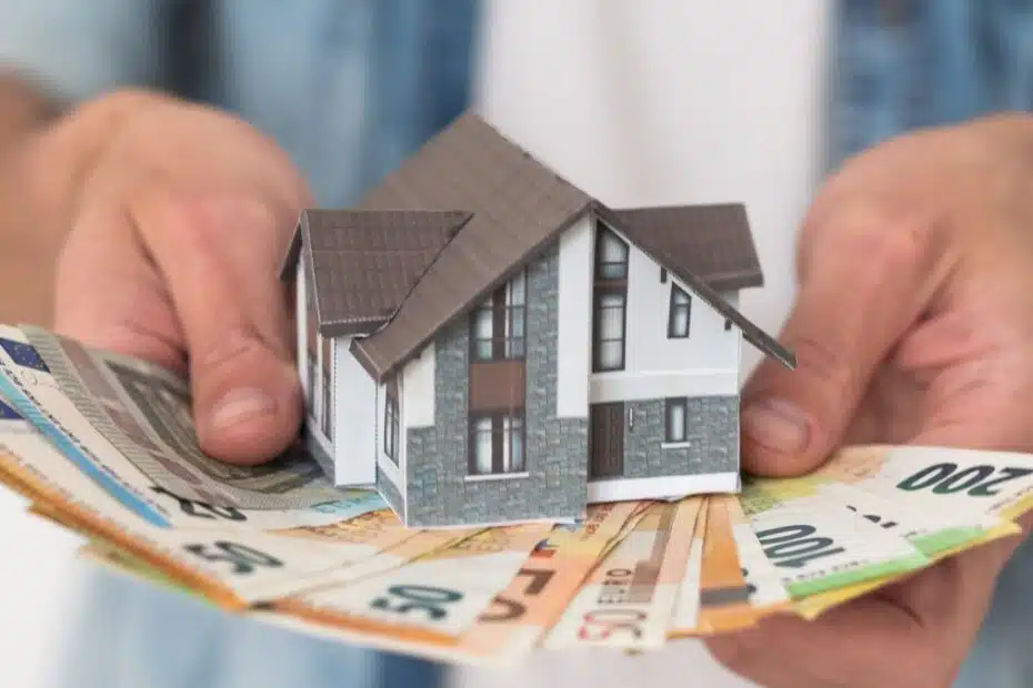 Hände halten ein Muster-Eigenheim auf Euro-Banknoten als Baufinanzierung