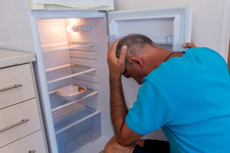 Verzweifelter Mann schaut in leeren Kühlschrank