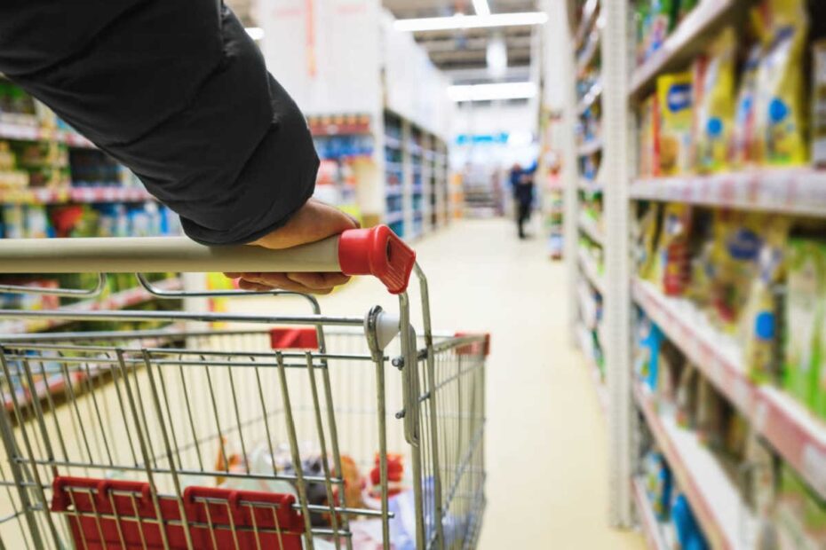 Person schiebt halbleeren Einkaufswaagen durch Supermarkt