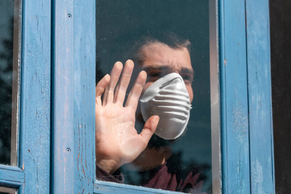 Mann mit Gesichtsmaske schaut aus einem Fenster