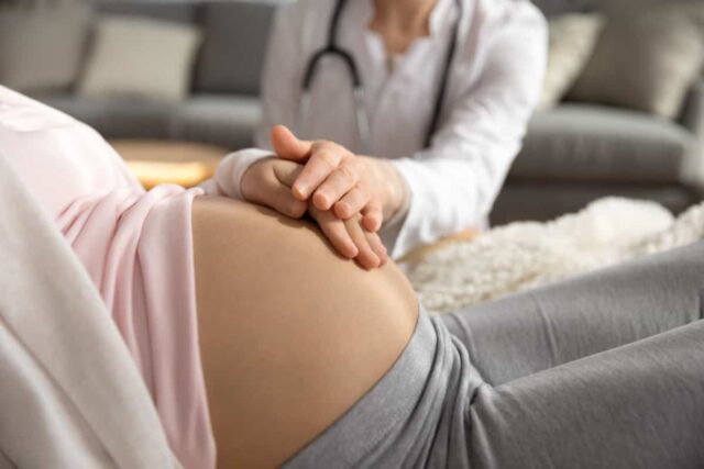 Ärztin untersucht den Bauch einer schwangeren Frau