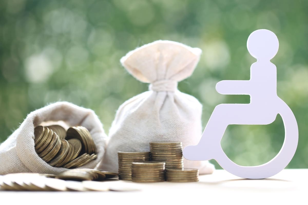 Rollstuhl-Figur neben Säckchen mit Münzen, symbolisch für Zuschuss bei Behinderung