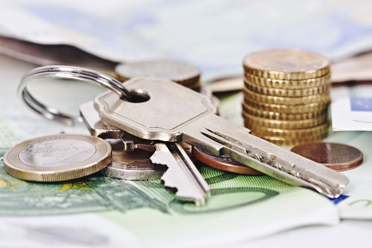 Wohnungsschlüssel und Münzstapel auf einigen Geldscheinen, symbolisch für Mietkaution