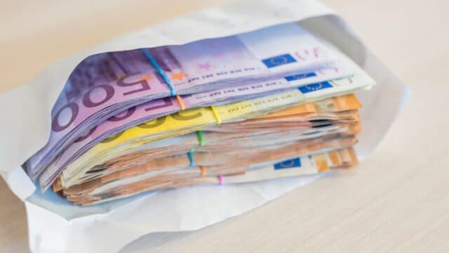 Nahaufnahme eines Umschlags, gefüllt mit einem großen Stapel von Euro-Banknoten, symbolisiert illegalen Bürgergeld-Betrug und Profit.