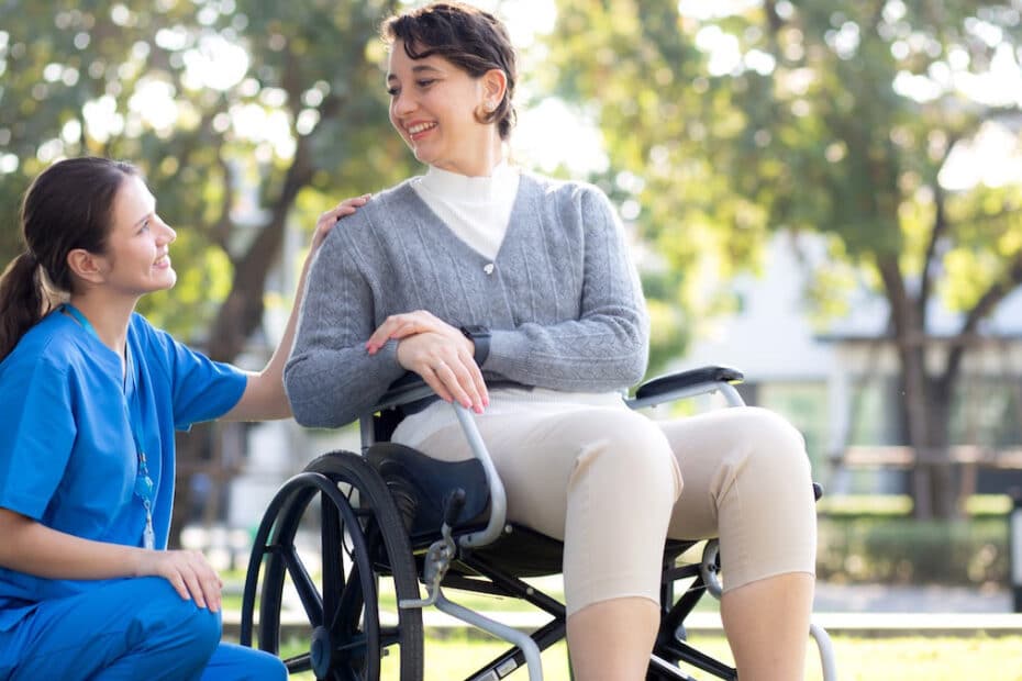 Junge Frau im Rollstuhl mit ihrer Pflegerin an der Seite