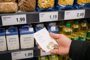 Hand hält Einkaufszettel und Münzen vor Preisetiketten im Supermarkt