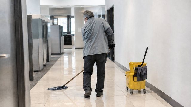 Reinigungskraft wischt allein einen Bürogang als Sinnbild für niedrige Rente trotz jahrzehntelanger Vollzeitarbeit