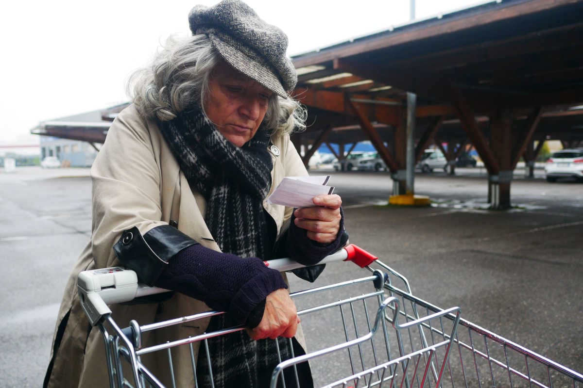 Ältere Frau traurig mit Einkaufszettel und Einkaufswagen