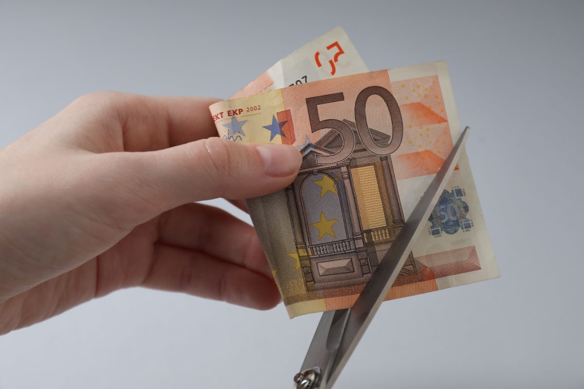 Hand hält 50 Euro schein und schneidet mit einer Schere hinein, symbolisch für Kürzung des Jobcenters