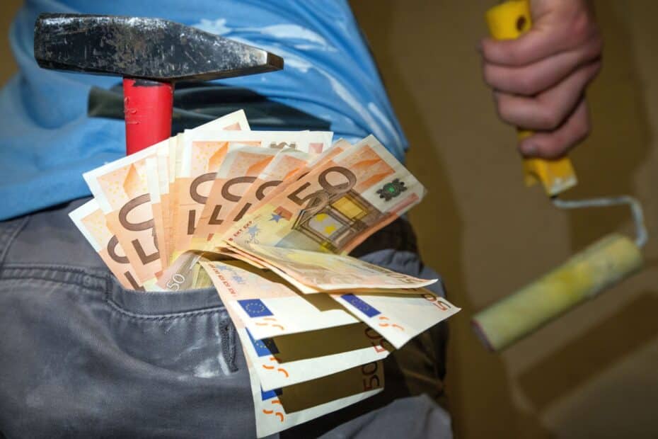 Schwarzarbeit in Deutschland: Handwerker auf Baustelle mit Hammer und Farbrolle, mehrere 50‑Euro‑Scheine stecken als Barlohn sichtbar aus der Hosentasche