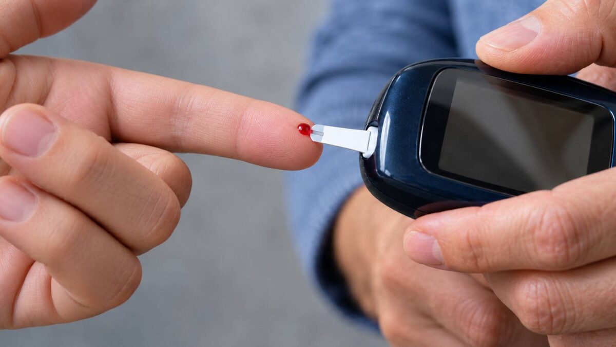 Nahaufnahme Hände bei einer Blutzuckermessung mit Teststreifen am Finger.