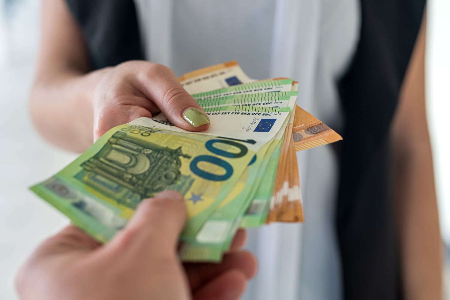 Nahaufnahme einer Hand, die ein Bündel 100-Euro-Scheine übergibt - Symbolbild für Bürgergeld-Auszahlung