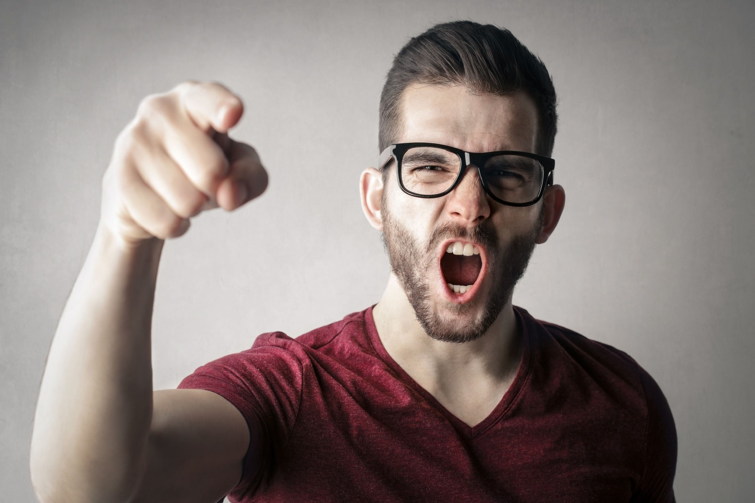 Ein junger Mann mit Brille schreit wütend und zeigt mit dem Finger nach vorn – Symbolbild für Stimmungsmache und Anschuldigungen in der Bürgergeld-Debatte.