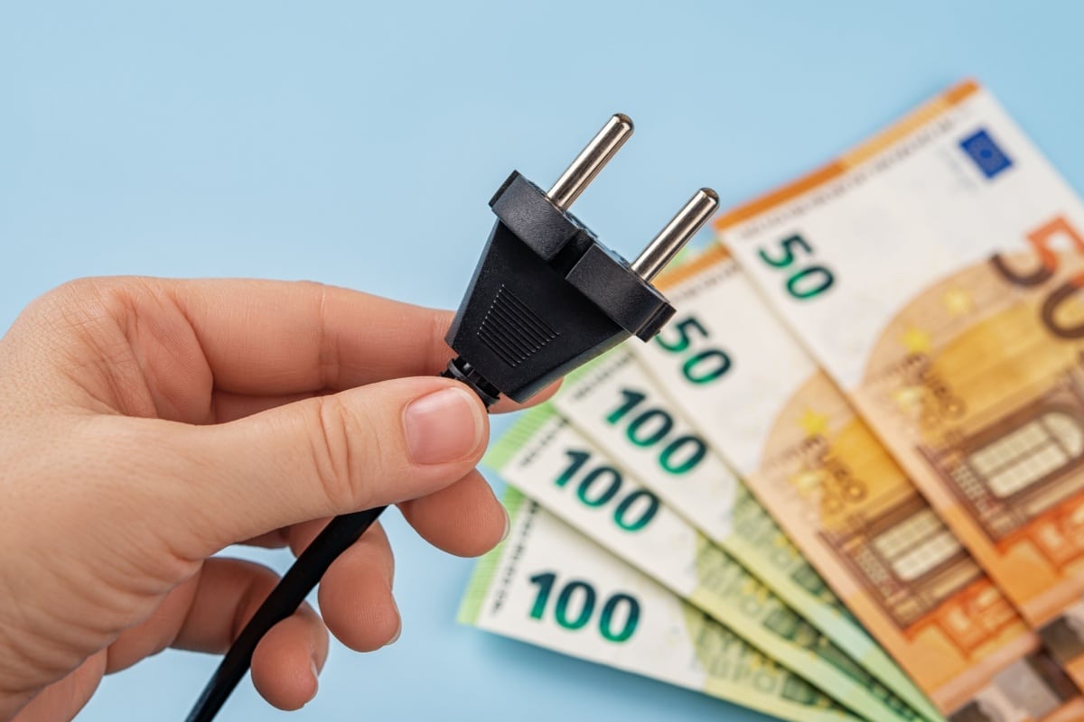 Hand hält einen schwarzen Stromstecker über Euro-Banknoten. Symbolbild für Stromkosten und Energieausgaben im Bürgergeld-Bezug.