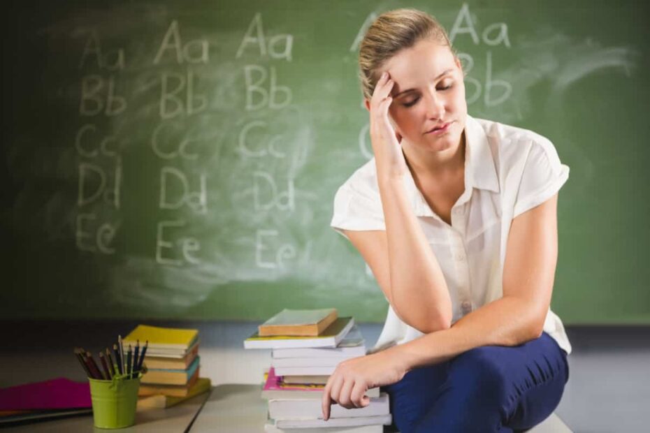 verzweifelte angehende Lehrerin sitzt auf Schreibtisch vor Tafel in der Schule