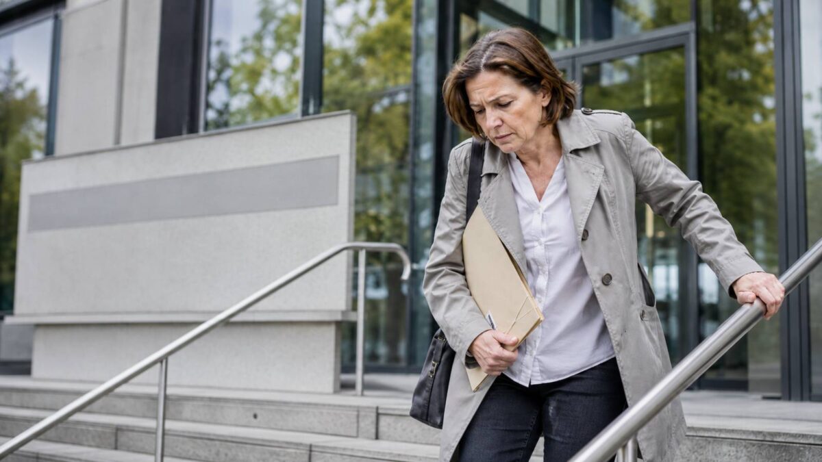 Frau mit Aktenmappe steigt vor einem Gerichtsgebäude vorsichtig eine Treppe hinab – trotz positiver Gutachten wurde ihre Erwerbsminderungsrente nicht weiterbewilligt.