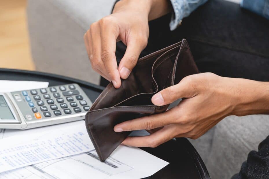 Hände halten leere Geldbörse, auf dem Tisch liegen Rechnungen und ein Taschenrechner