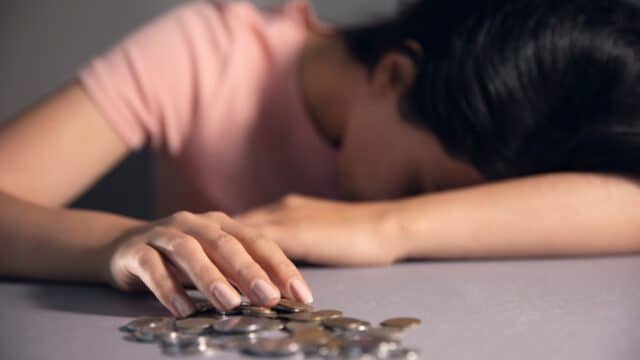 Verzweifelte Person mit Kopf auf dem Tisch und Euro-Münzen, symbolisiert Armut und Schulden.